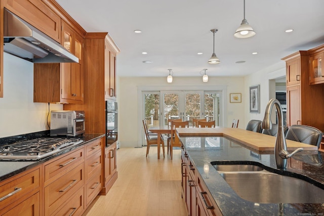 kitchen featuring oven, a sink, stainless steel gas stovetop, pendant lighting, and under cabinet range hood