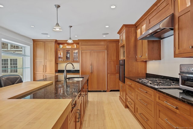 kitchen featuring stainless steel gas cooktop, a sink, pendant lighting, brown cabinetry, and under cabinet range hood