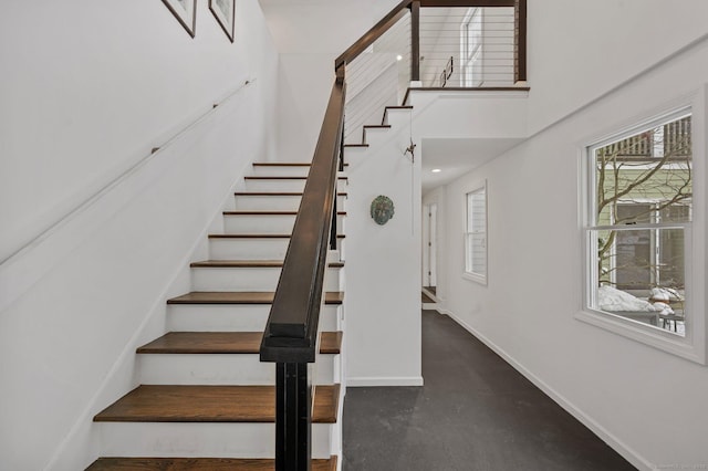 stairway with baseboards, a high ceiling, and finished concrete flooring