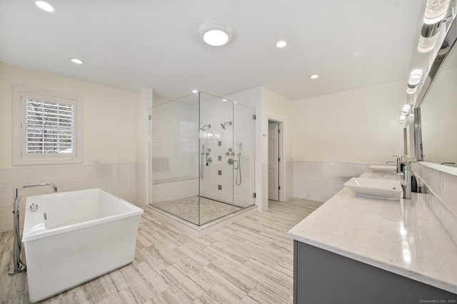 full bath featuring a shower stall, a sink, a freestanding tub, tile walls, and double vanity