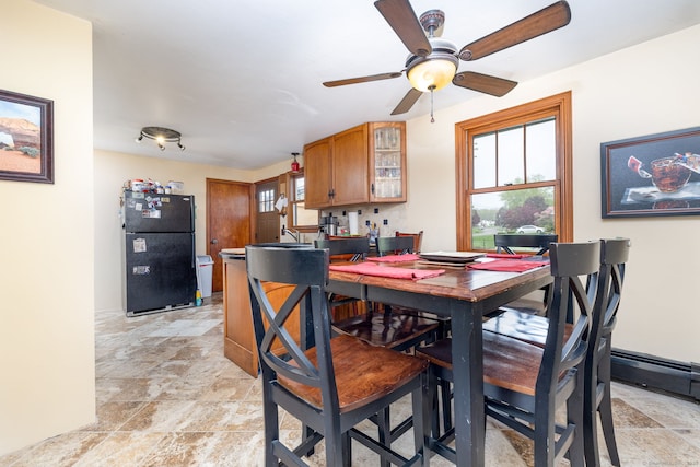 dining area with a baseboard radiator, a wealth of natural light, a ceiling fan, and stone finish flooring