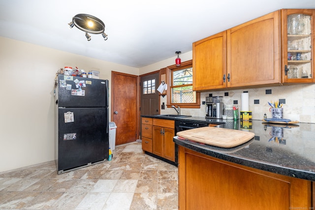 kitchen featuring freestanding refrigerator, backsplash, brown cabinetry, and glass insert cabinets