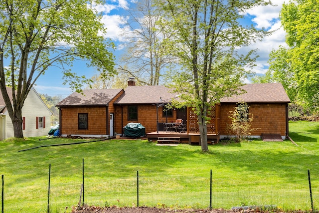 rear view of house featuring a chimney, a wooden deck, fence, a shingled roof, and a yard