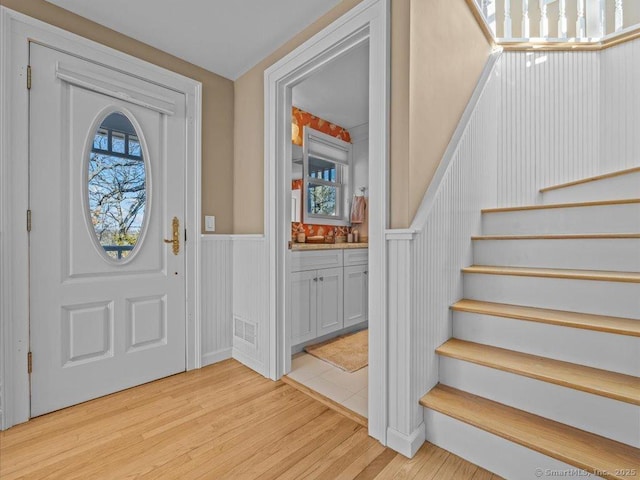 50 Grove Way, Clinton, CT 06413 - entrance foyer featuring light wood finished floors, a wainscoted wall, visible vents, stairway, and a decorative wall