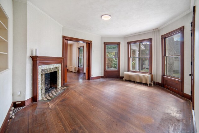 unfurnished living room with baseboards, radiator, wood finished floors, and crown molding