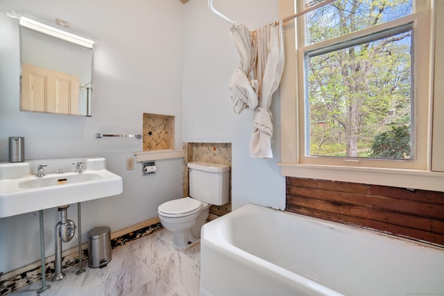 full bathroom featuring toilet, a healthy amount of sunlight, a tub to relax in, and marble finish floor