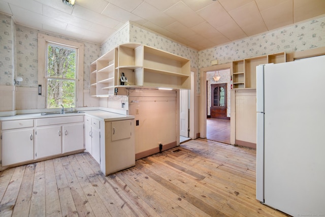 kitchen with open shelves, light wood-style flooring, a sink, wallpapered walls, and freestanding refrigerator