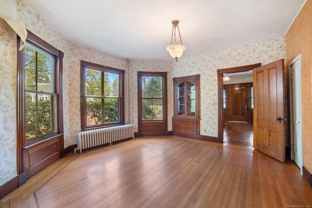 empty room featuring radiator heating unit, wood finished floors, and wallpapered walls