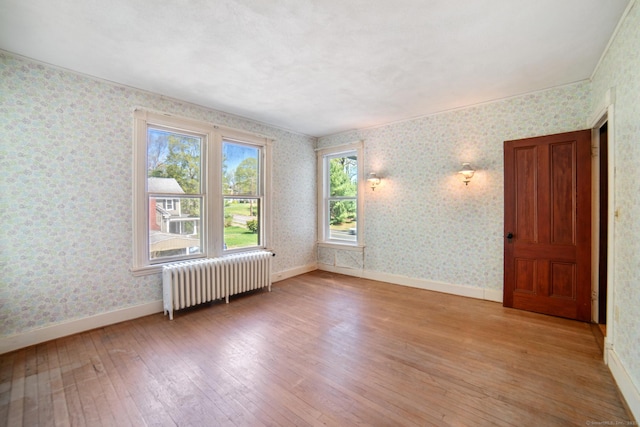 unfurnished room with wallpapered walls, radiator heating unit, light wood-style flooring, and baseboards