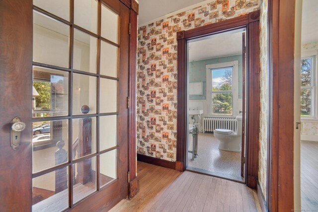 doorway featuring wallpapered walls, radiator heating unit, hardwood / wood-style floors, and baseboards