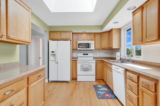 kitchen featuring backsplash, a sink, light wood-style flooring, and white appliances