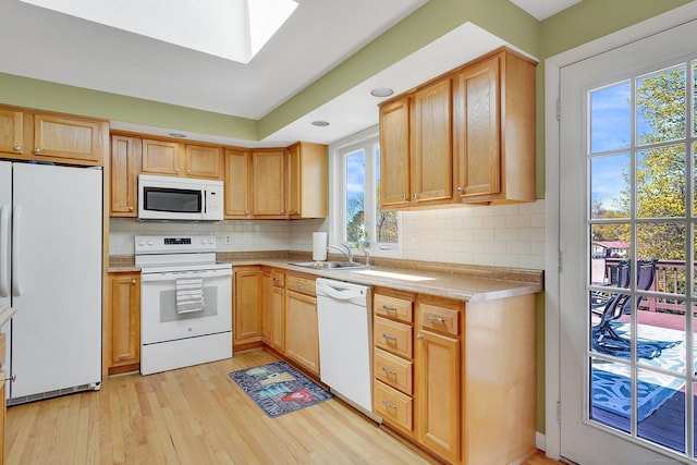 kitchen with white appliances, light wood-type flooring, tasteful backsplash, light countertops, and a skylight