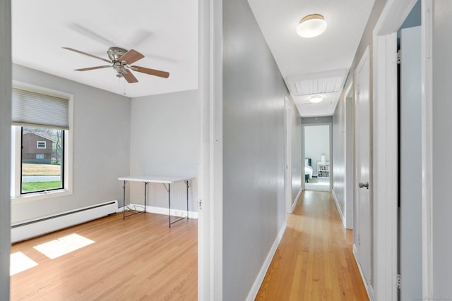 hallway featuring attic access, light wood finished floors, baseboards, and a baseboard radiator