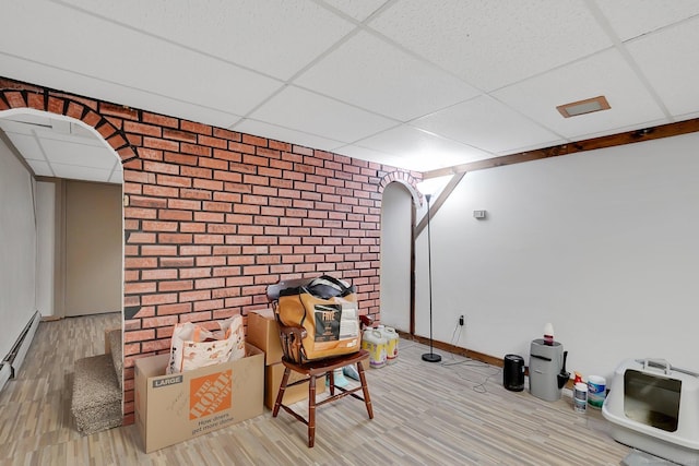 unfurnished room featuring wood finished floors, arched walkways, brick wall, and a drop ceiling