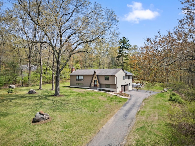 view of front facade featuring a front lawn, aphalt driveway, a garage, a chimney, and a forest view