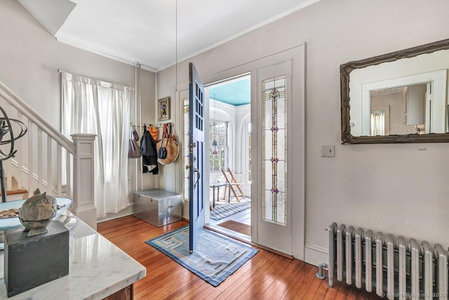 entryway with radiator heating unit, crown molding, stairs, and wood-type flooring