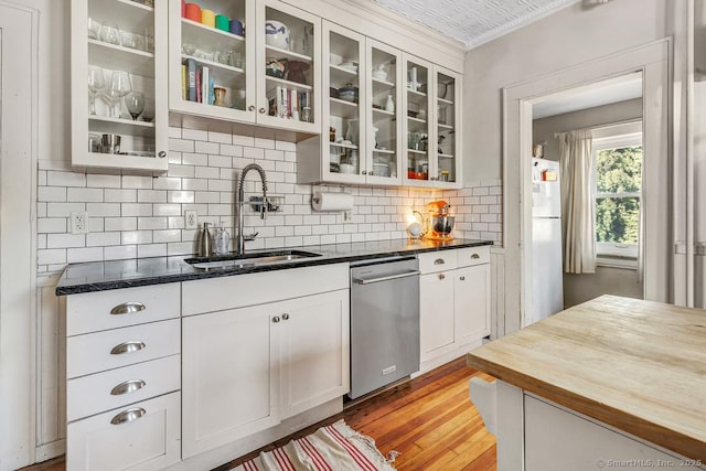 kitchen with stainless steel dishwasher, butcher block countertops, decorative backsplash, a sink, and light wood-type flooring