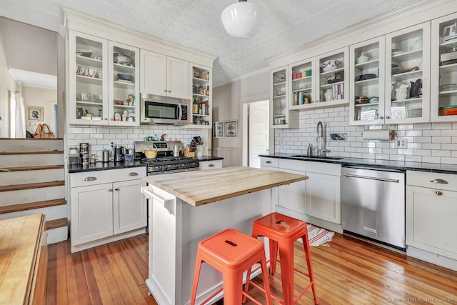 kitchen with butcher block countertops, decorative backsplash, stainless steel appliances, light wood-style floors, and a sink