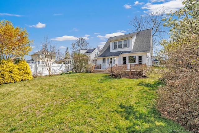 back of property with a wooden deck, a yard, and fence
