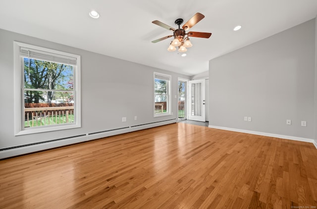 spare room with wood finished floors, a ceiling fan, a healthy amount of sunlight, and a baseboard radiator