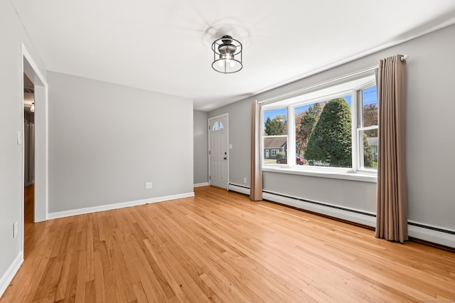 spare room featuring light wood-type flooring, a baseboard radiator, and baseboards