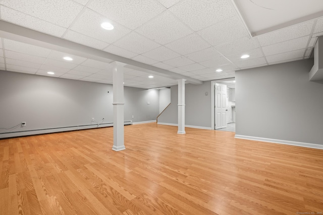 finished below grade area with baseboards, a drop ceiling, and light wood-type flooring