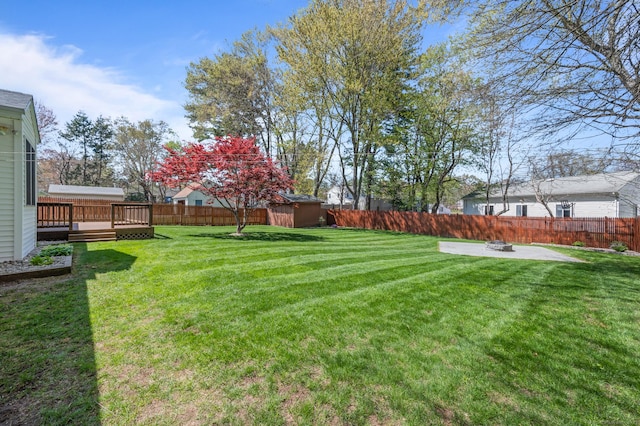 view of yard with a storage shed, a deck, an outbuilding, a fenced backyard, and an outdoor fire pit