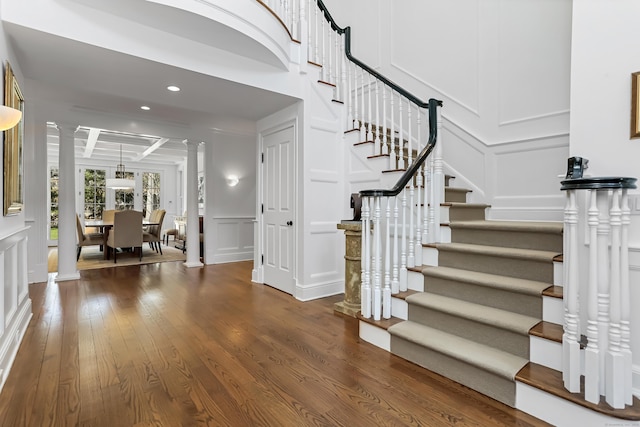 staircase with beamed ceiling, recessed lighting, decorative columns, a decorative wall, and wood finished floors