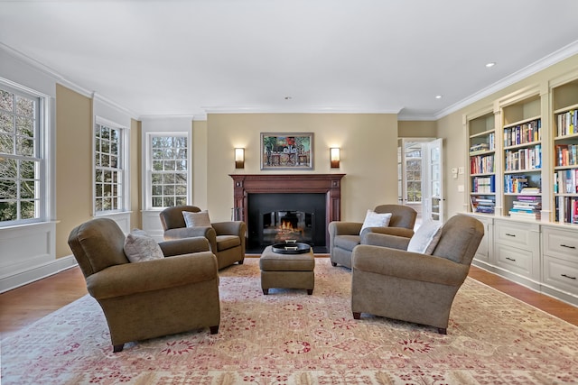 living room with ornamental molding, a glass covered fireplace, a healthy amount of sunlight, and light wood-style floors