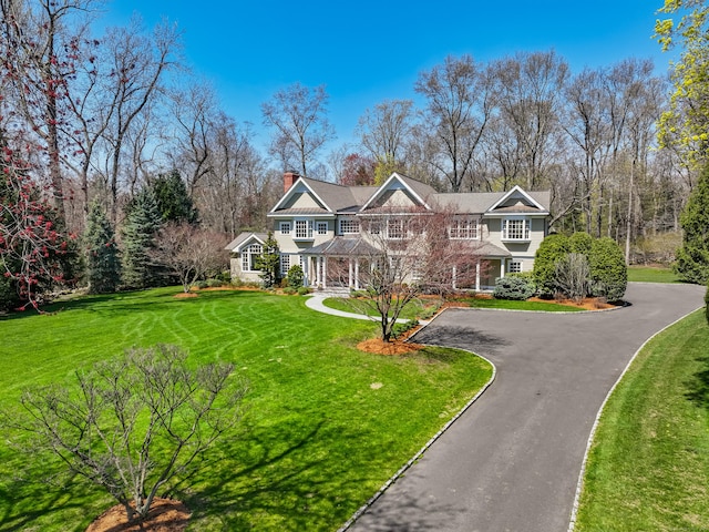 shingle-style home featuring a chimney, driveway, and a front yard
