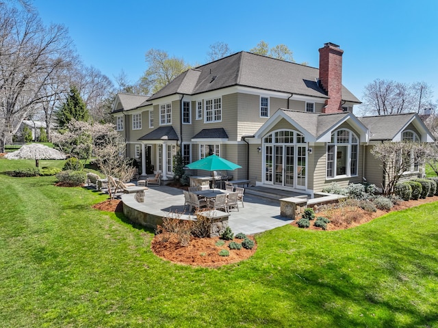 back of house with a chimney, a yard, a patio, roof with shingles, and french doors