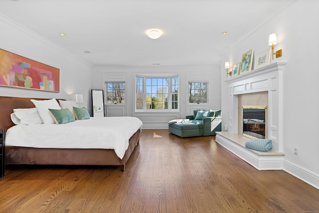 bedroom featuring a glass covered fireplace, wood finished floors, ornamental molding, and baseboards
