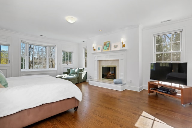 bedroom with ornamental molding, a high end fireplace, visible vents, and wood finished floors