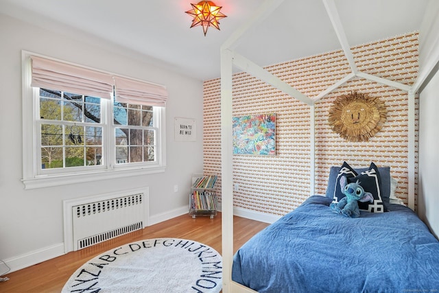 bedroom with radiator, wood finished floors, and baseboards