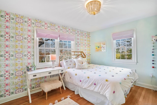 bedroom with an inviting chandelier, wallpapered walls, wood finished floors, and baseboards