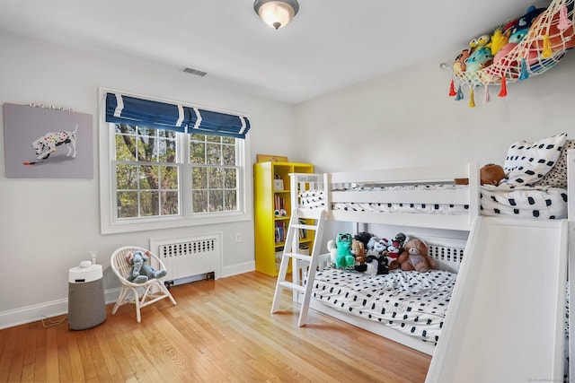 bedroom with baseboards, radiator heating unit, visible vents, and hardwood / wood-style floors