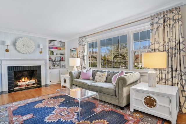 living room featuring crown molding, built in shelves, wood finished floors, and a fireplace