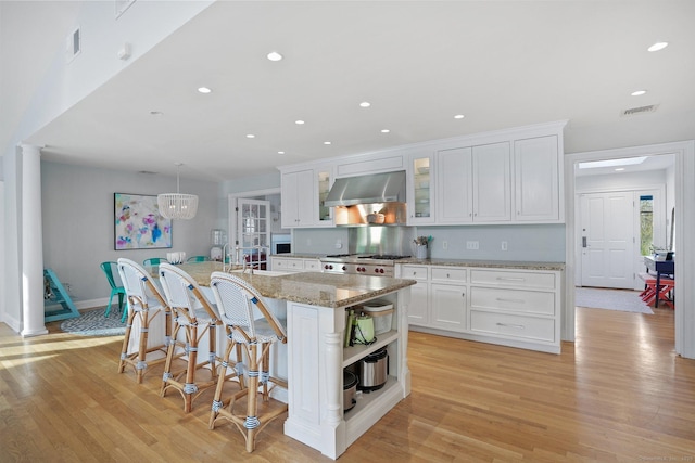 kitchen featuring open shelves, light wood-type flooring, a breakfast bar area, ventilation hood, and white cabinets