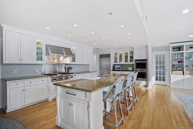 kitchen featuring a kitchen breakfast bar, white cabinetry, light wood finished floors, ventilation hood, and high quality appliances