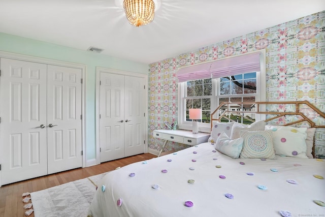 bedroom featuring wood finished floors, two closets, wallpapered walls, baseboards, and visible vents
