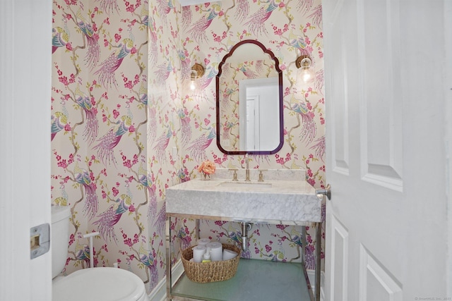 bathroom with wallpapered walls, toilet, and a sink