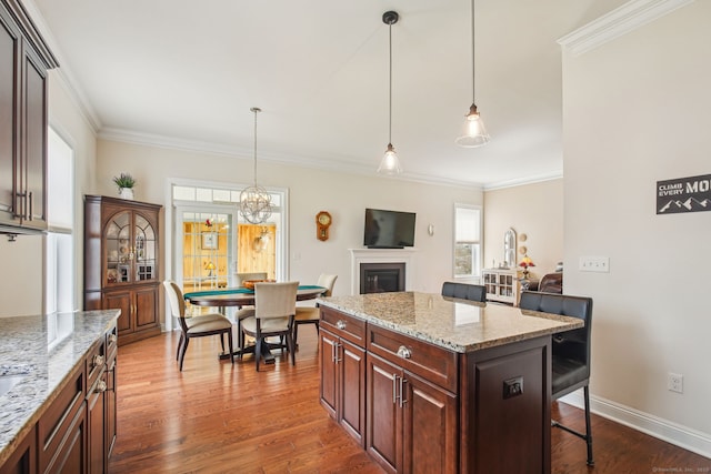 kitchen with dark wood-style flooring, a fireplace, a breakfast bar area, and crown molding