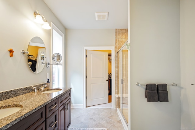 full bathroom with a sink, a walk in closet, a stall shower, double vanity, and baseboards