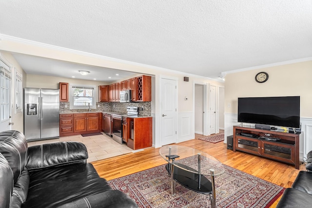 living area featuring light wood-style floors, a wainscoted wall, ornamental molding, and a textured ceiling