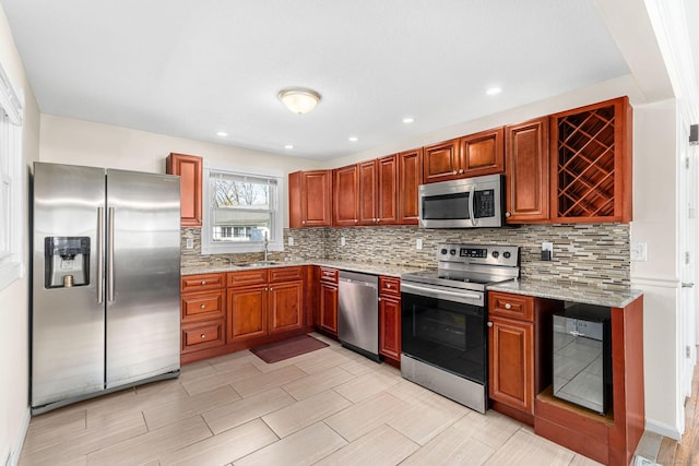 kitchen featuring light stone countertops, appliances with stainless steel finishes, a sink, tasteful backsplash, and wine cooler