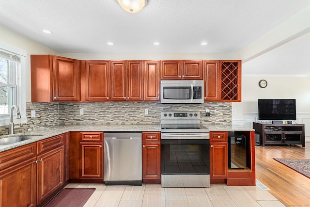 kitchen featuring a sink, appliances with stainless steel finishes, light stone counters, and beverage cooler