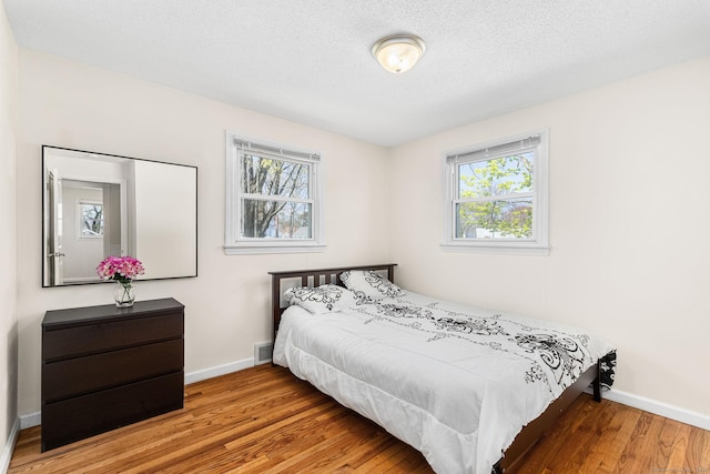 bedroom with baseboards, a textured ceiling, and wood finished floors