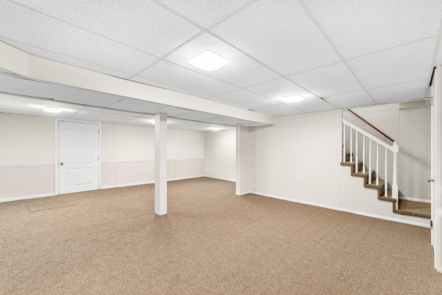 finished basement featuring baseboards, carpet, a drop ceiling, and stairway
