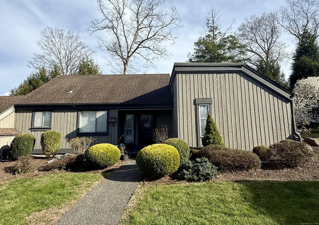 mid-century modern home with board and batten siding, a shingled roof, and a front lawn