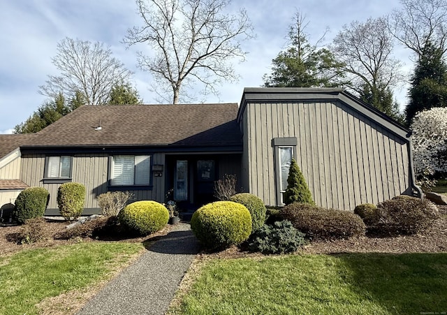 mid-century modern home with board and batten siding, a shingled roof, and a front lawn